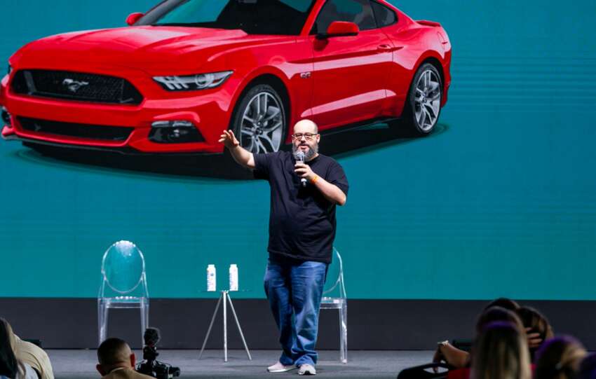 RIcardo Cavallini no palco à frente de uma imagem de um carro vermelho