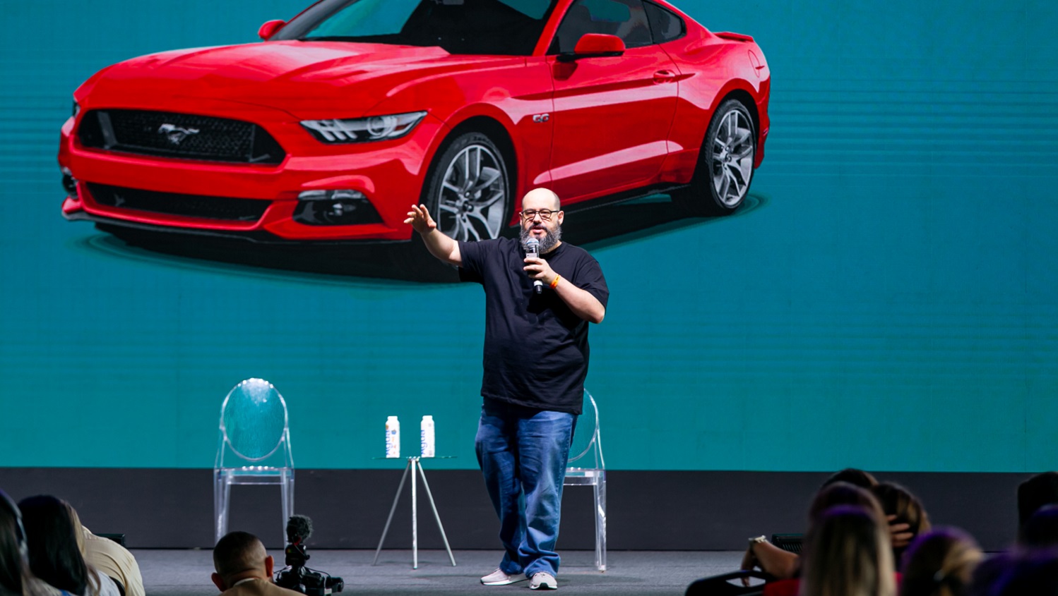 RIcardo Cavallini no palco à frente de uma imagem de um carro vermelho