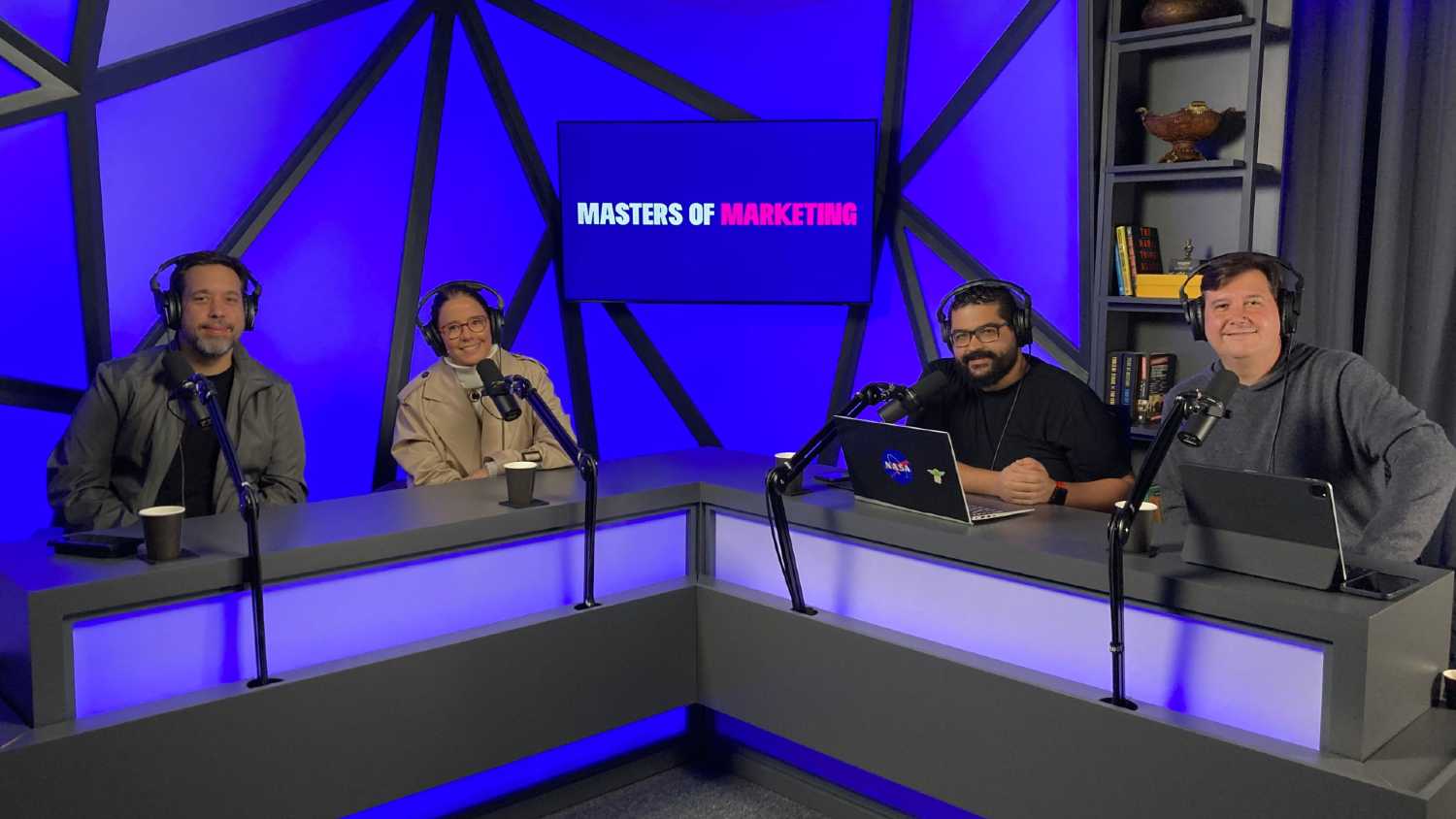 4 pessoas no estúdio, sentados atrás de uma bancada, gravando podcast